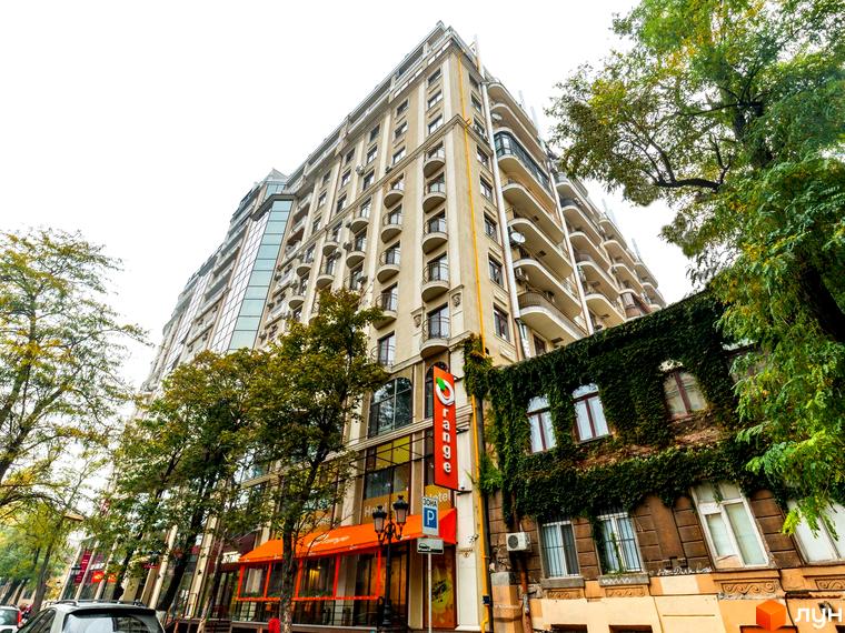 Фасад житлового комплексу Будинок №1 з балконами та скляними елементами. Зелені насадження та дерева біля будівлі.