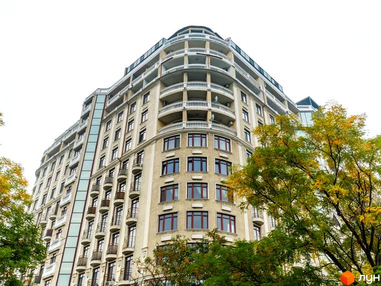 Будинок №1 - це багатоповерховий житловий комплекс з вигнутими балконами та великою кількістю вікон. Навколо будівлі ростуть дерева з осіннім листям.