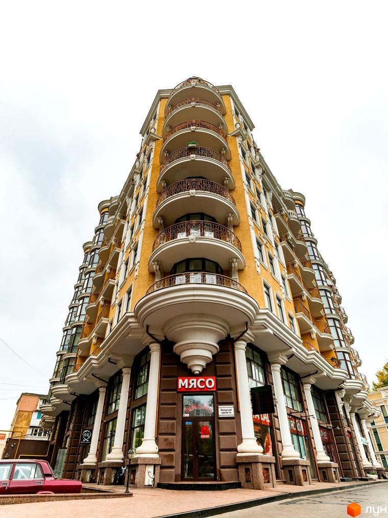 Вигляд житлового комплексу ЖК Крит з балконами та колонами на фасаді. Прибудинкова територія з пішохідними доріжками та зеленими насадженнями.