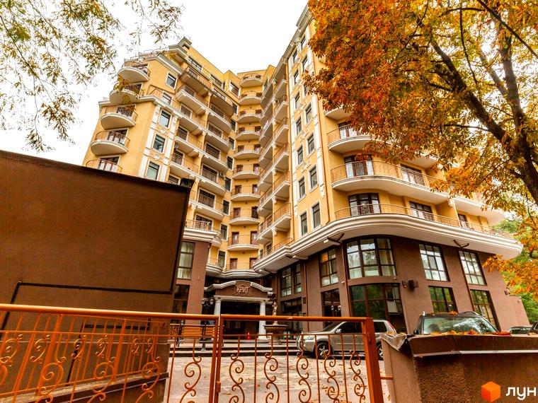 Житловий комплекс Крит з фасадом жовтого кольору та балконами. Прибудинкова територія з зеленими насадженнями та паркувальними місцями.