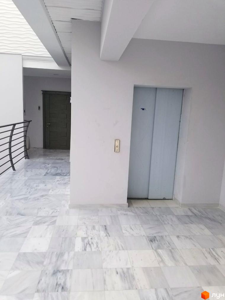 Житловий комплекс Santorini. Просторий коридор з мармуровою підлогою та ліфтом. Світлі стіни та двері створюють відчуття простору та світла.