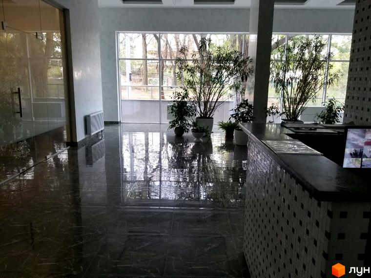 Інтер'єр холу в ЖК Санторіні. Просторий хол з глянцевою підлогою, скляними дверима та великими вікнами, що відкривають вид на зелені насадження.