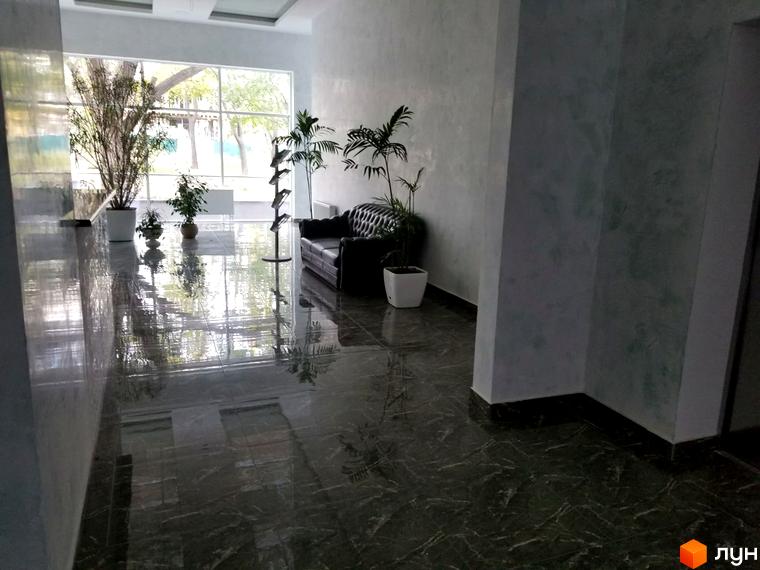 Інтер'єр ЖК Санторіні. Просторий хол з рослинами, диваном та великими вікнами. Глянцева підлога відображає навколишнє середовище.