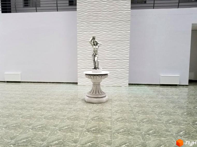 Інтер'єр холу в ЖК Санторіні з скульптурою на постаменті. Просторий зал з світлими стінами та підлогою з плиткою.
