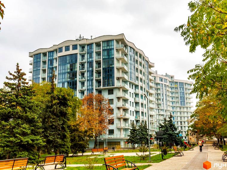 Житловий комплекс Santorini з панорамними вікнами та балконами. Зелена прибудинкова територія з лавками для відпочинку.