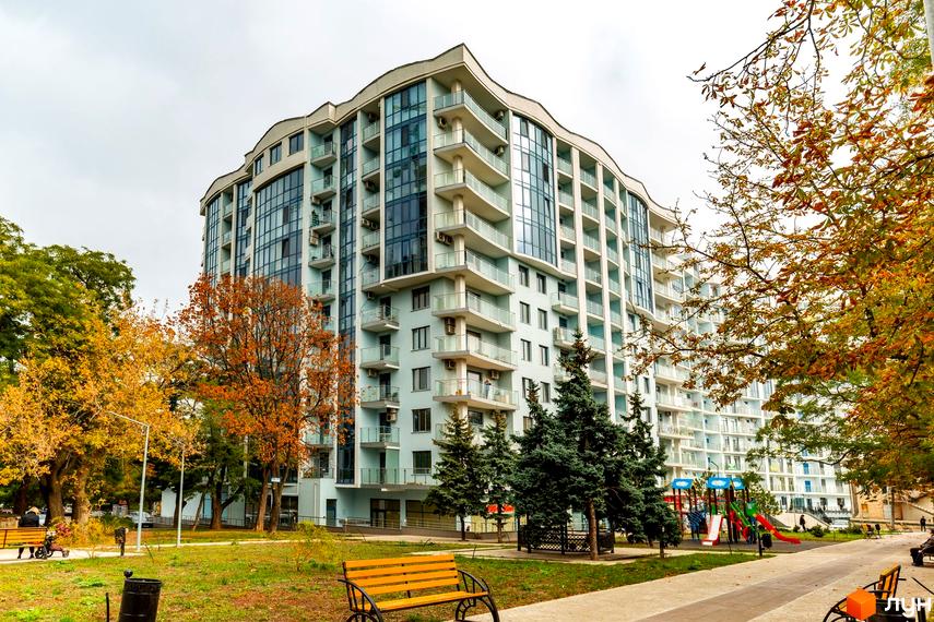 Житловий комплекс Santorini. Висотна будівля з балконами та скляними фасадами. На території є дитячий майданчик, лавки та зелені насадження.