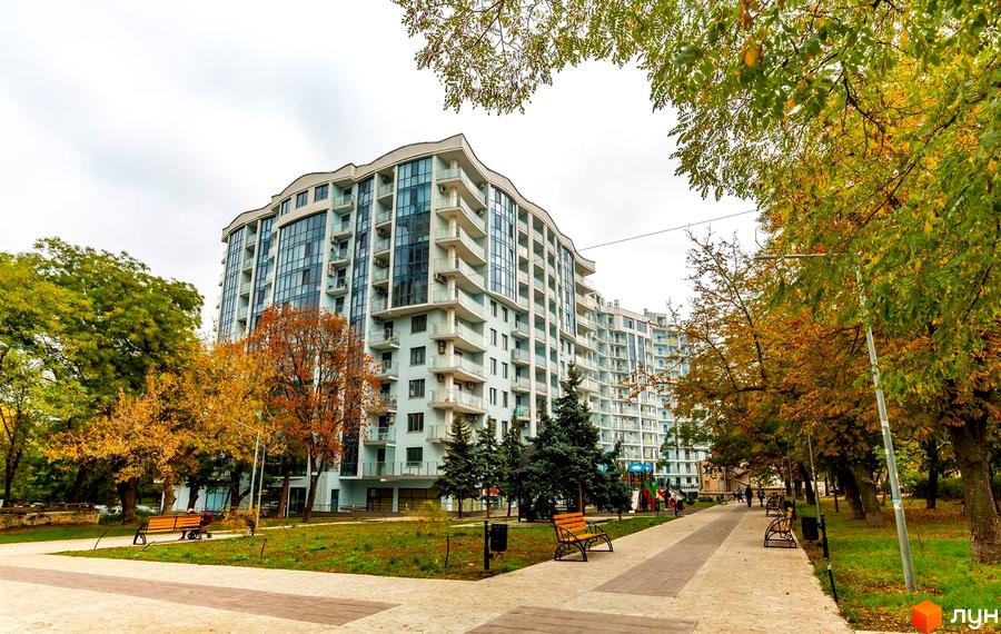 Житловий комплекс Santorini. Висотна будівля з великими вікнами та балконами. На території є доріжки для прогулянок, лавки та дерева.