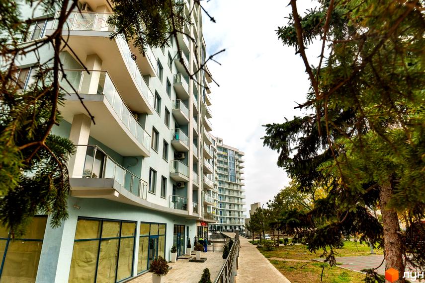 Житловий комплекс Santorini. Високі будинки з балконами та скляними огорожами. На передньому плані дерева, тротуар та прибудинкова територія.