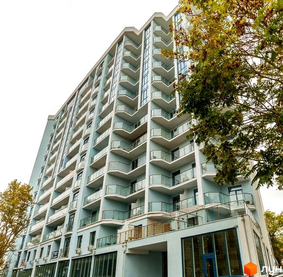 Висотна будівля ЖК Санторіні з балконами та скляними огородженнями. На передньому плані видно зелені насадження та вхідну групу з панорамними вікнами.