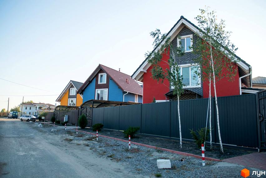 Вигляд на Котеджне містечко Osocor Scandi House з різнокольоровими будинками та сірим парканом. Навколо будинків ростуть дерева та кущі.