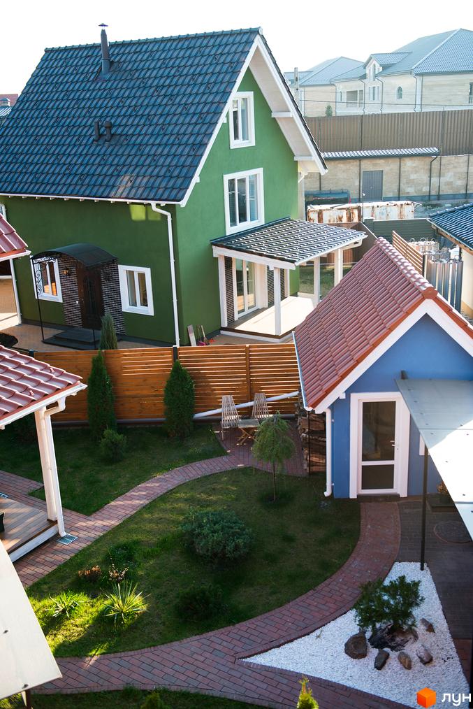 Вигляд на котеджне містечко Osocor Scandi House: зелений будинок з темним дахом та синій будинок з червоним дахом, оточені брукованими доріжками та зеленою територією.