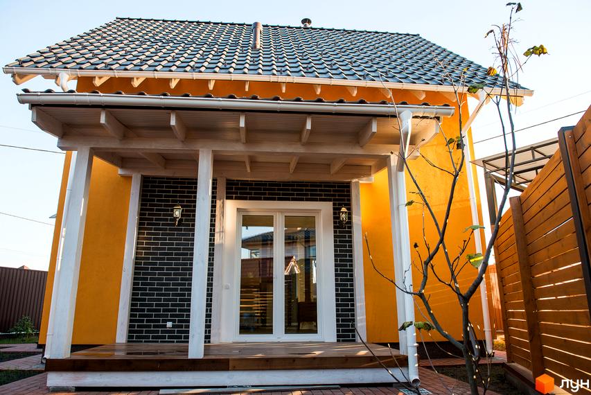 Вигляд будинку в Котеджному містечку Osocor Scandi House з терасою та двоповерховими вікнами. Подвір'я з декоративними деревами та доріжками.