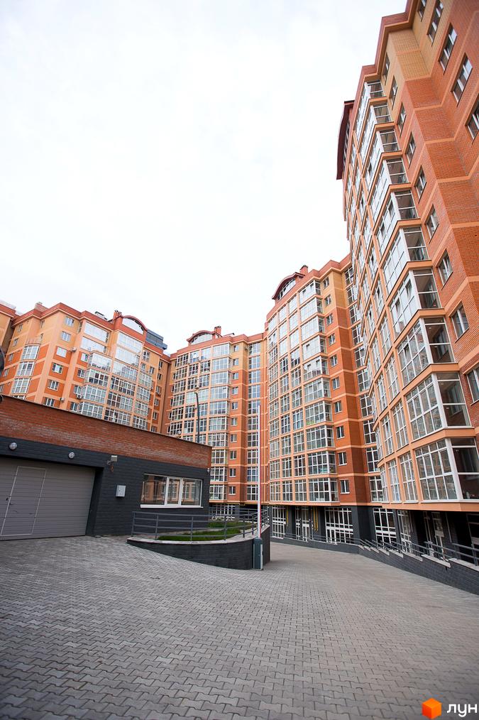 Житловий комплекс Перспектива: багатоповерхові будинки з цегляними фасадами та заскленими балконами. Прибудинкова територія з бруківкою та в'їздом до паркінгу.