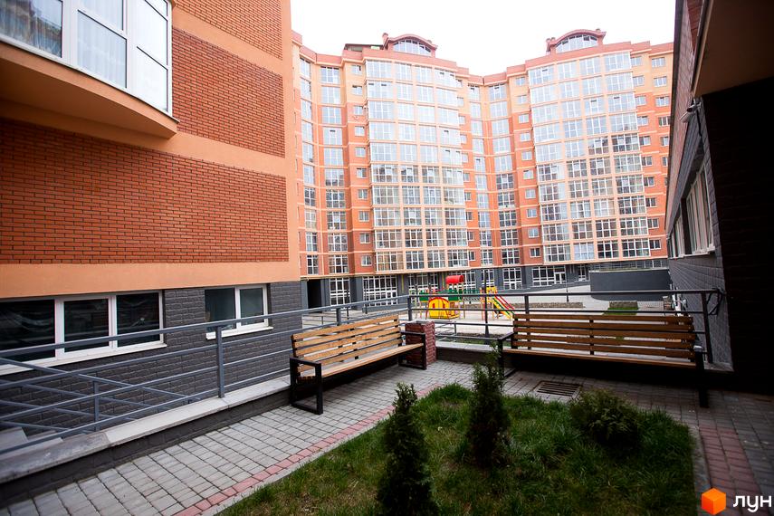 Багатоповерховий житловий будинок ЖБК Перспектива з помаранчево-цегляним фасадом та великими вікнами. На прибудинковій території облаштовано дитячий майданчик та лавки для відпочинку.