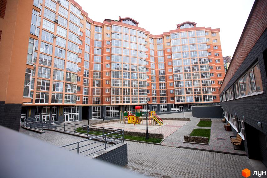 Новобудова ЖБК Перспектива: багатоповерховий будинок з помаранчевим фасадом та внутрішній двір з дитячим майданчиком і зеленими насадженнями.