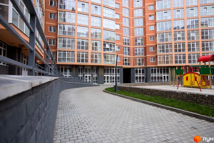 Багатоповерховий житловий будинок ЖБК Перспектива з цегляним фасадом та великими вікнами. На території бруківка, газон і дитячий майданчик.