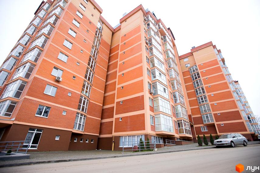 ЖБК Перспектива: будинок з помаранчевим цегляним фасадом, вікнами та заскленими балконами. Поруч дорога та зелені насадження.