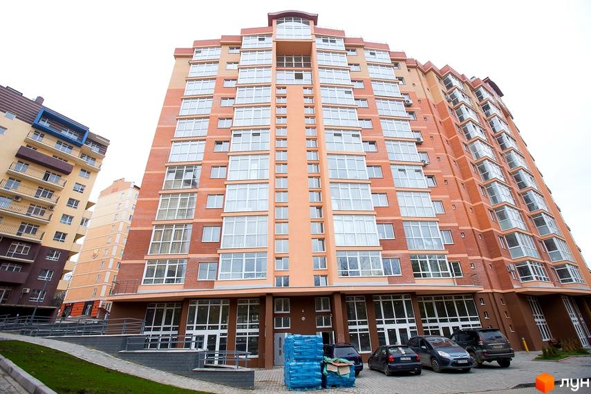 Багатоповерховий будинок ЖБК Перспектива з цегляним фасадом та великими вікнами. Навколо будинку облаштована територія з пішохідними доріжками та парковкою для автомобілів.