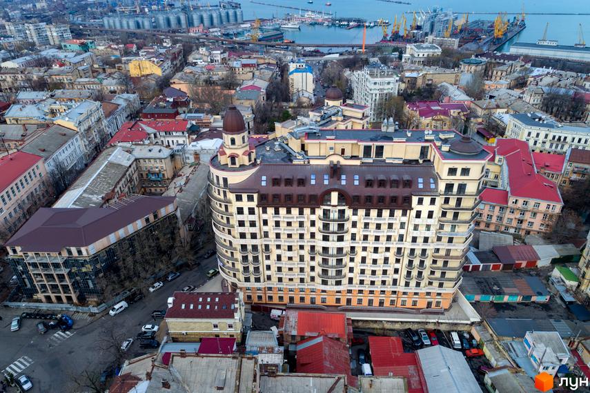 Житловий комплекс Наследие Дерибаса – багатоповерховий будинок зі світлим фасадом, балконами та коричневим дахом, розташований серед міської забудови з видом на порт.