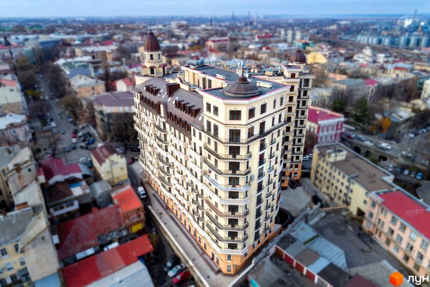 Житловий комплекс Наследие Дерибаса: багатоповерхова будівля зі світлим фасадом, коричневим дахом та балконами. Видно міську забудову та дороги.