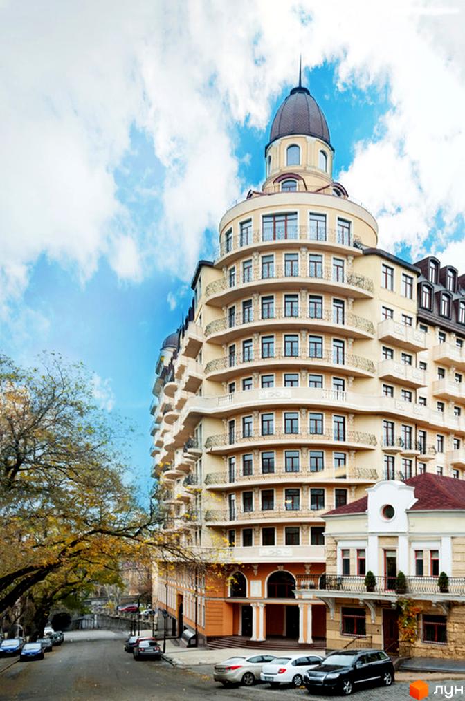 Житловий комплекс Наследие Дерибаса з елегантною архітектурою та балконами. Прибудинкова територія з парковими зонами та автомобілями.