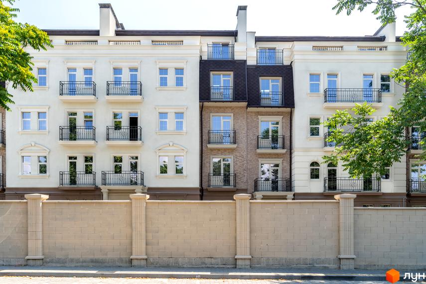 Зовнішній вигляд фасаду житлового комплексу CHELSEA Club House з балконами та вікнами. Перед будинком розташована цегляна стіна з колонами.