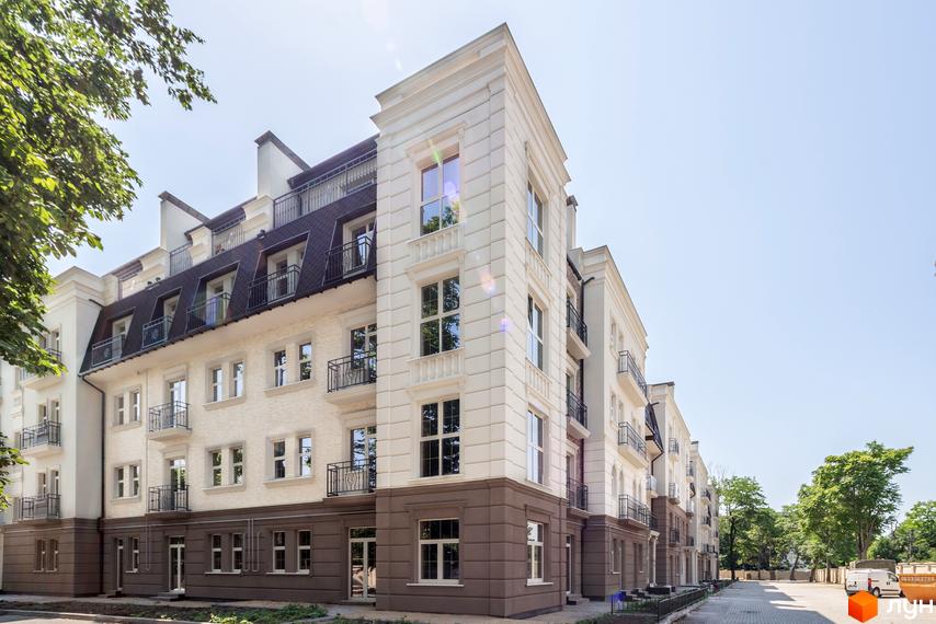 Фасад житлового комплексу CHELSEA Club House з білими декоративними елементами та темним дахом. Прибудинкова територія з деревами та парковкою.