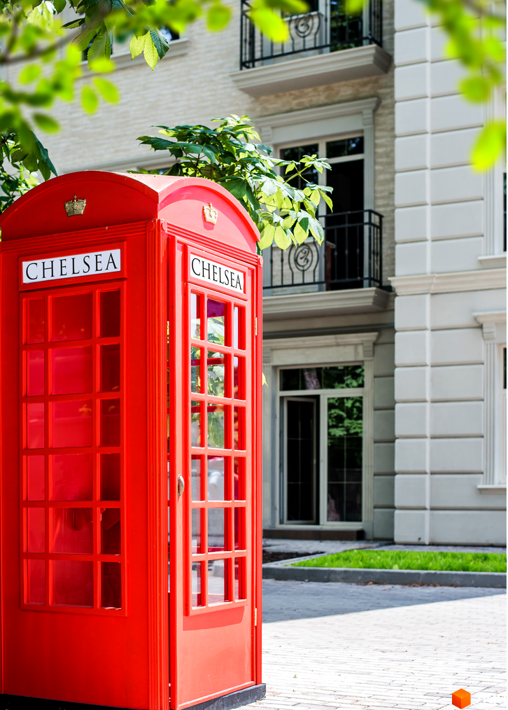 Житловий комплекс CHELSEA Club House з червоною телефонною будкою на фоні білої будівлі та зеленої трави. Зовнішній вигляд будинку та прибудинкова територія.