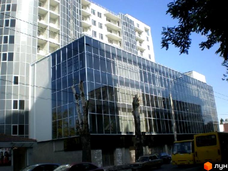 Житловий комплекс 5 елемент з великою скляною фасадною частиною та прибудинковою територією з деревами і автомобілями.