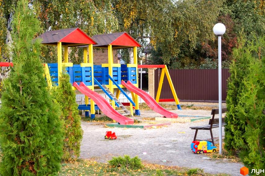 Дитячий майданчик у Містечку котеджів Вишневий хуторок. Яскравий ігровий комплекс з гірками та гойдалками для дітей, поруч лавка для відпочинку.