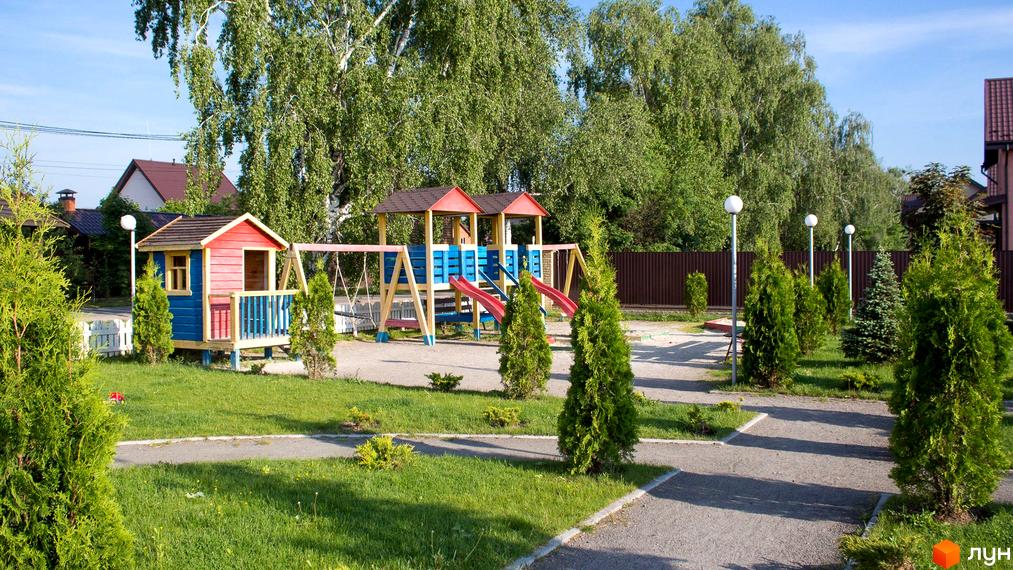 Дитячий майданчик у Котеджному містечку Вишневий хуторок. На території комплексу є дитячий будиночок, гойдалки та гірки. Навколо зелені насадження та доглянуті доріжки.