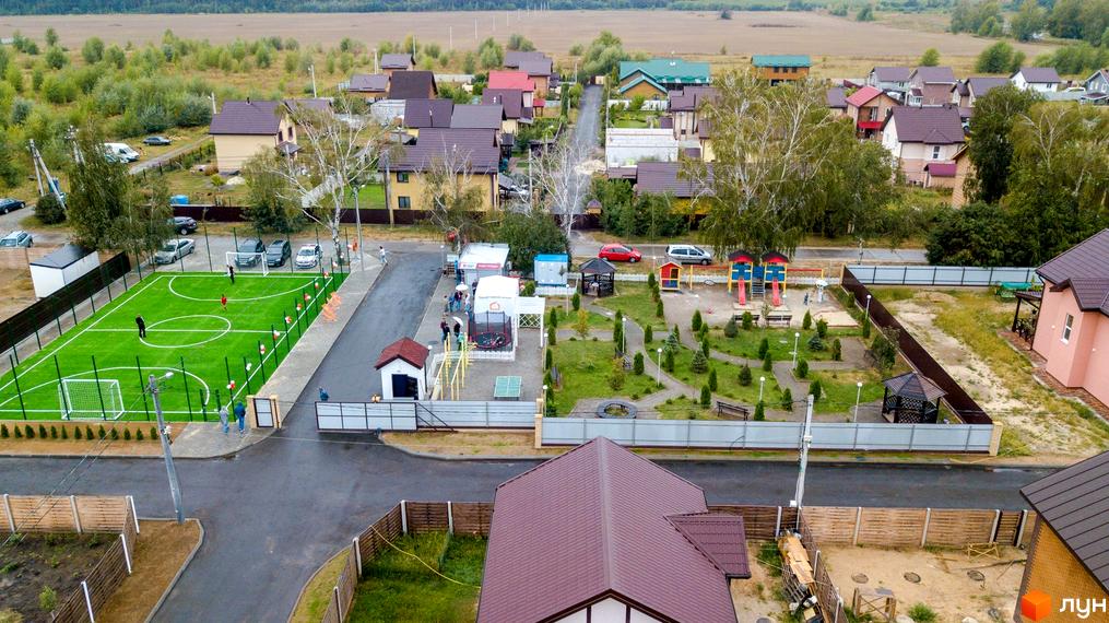 Вид на Котеджне містечко Вишневий хуторок з висоти пташиного польоту. На передньому плані будинок з коричневим дахом, поруч дитячий майданчик та футбольне поле.