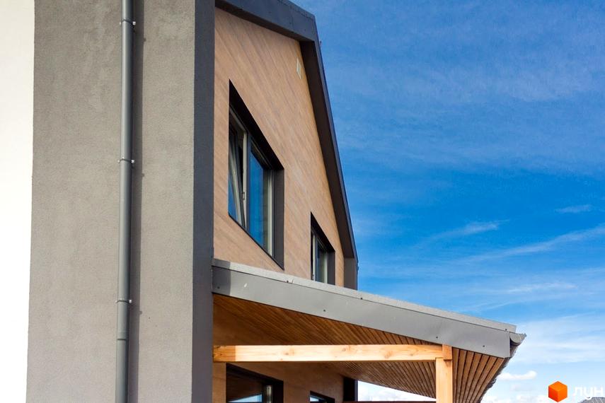 Частина фасаду будинку Котеджного містечка Нова Олександрівка з дерев'яним облицюванням, сірою штукатуркою та вікнами. Видно дерев'яний навіс.