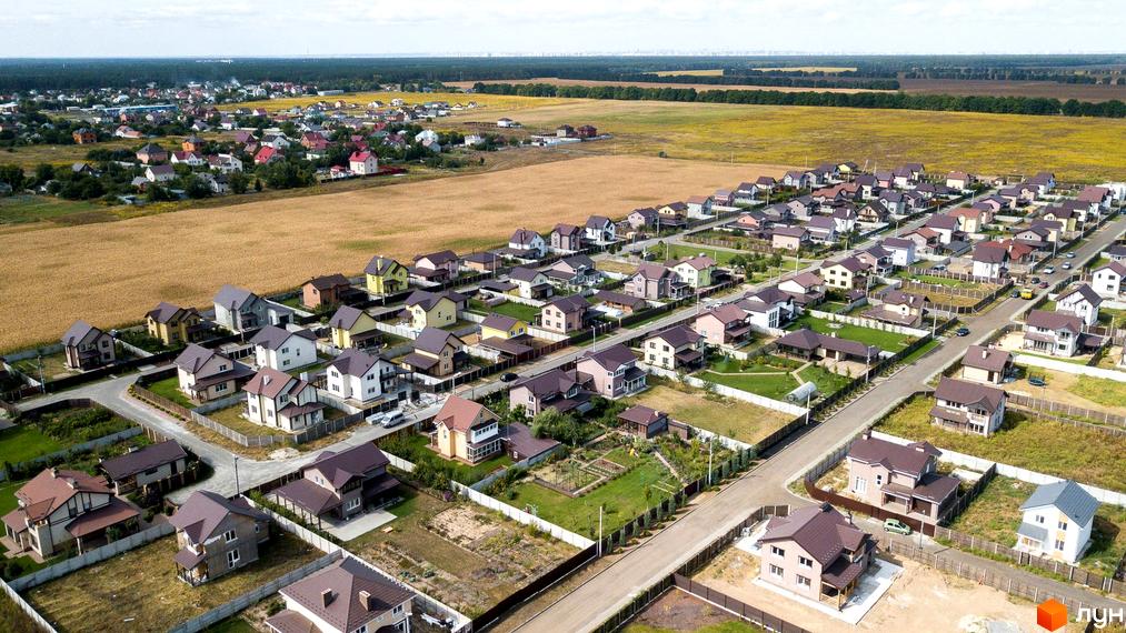 Котеджне містечко Нова Олександрівка: аерофото двоповерхових котеджів з різними фасадами та темними дахами. Територія має дороги, зелені газони та межує з полями.