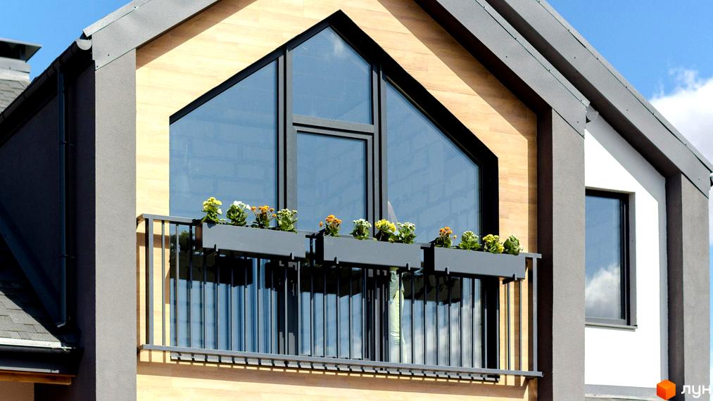 Фасад будинку Котеджного містечка Нова Олександрівка з великим трикутним вікном та балконом. На балконі встановлені квіткові ящики.