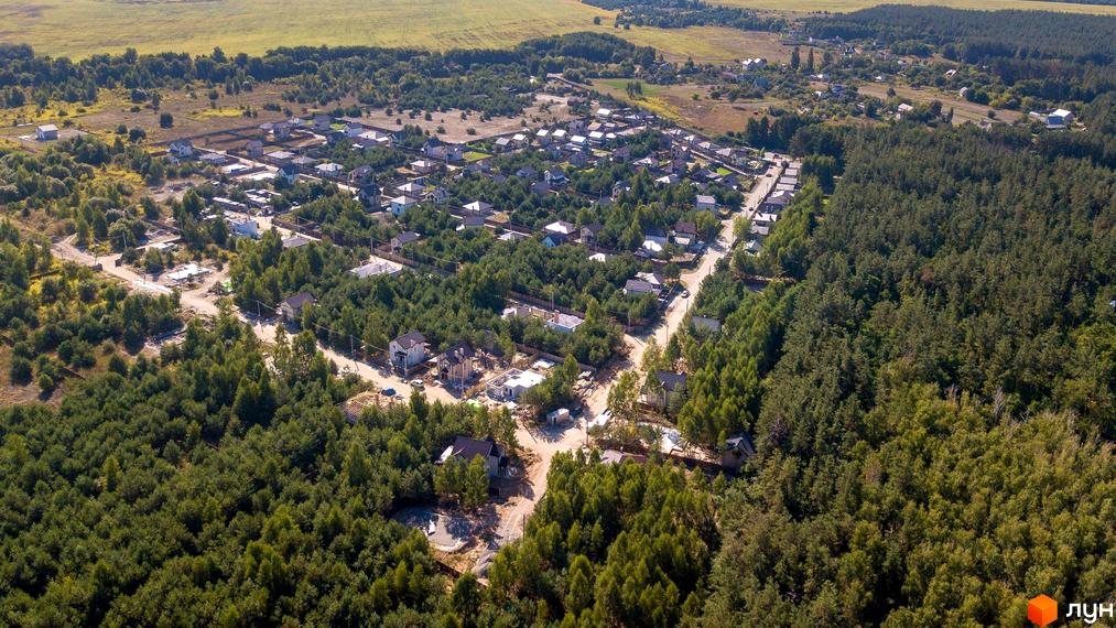 Вид зверху на котеджне містечко Лісове озеро. На зображенні видно будинки з різними дахами, розташовані серед дерев. Навколо будівель є зелені насадження та дороги.