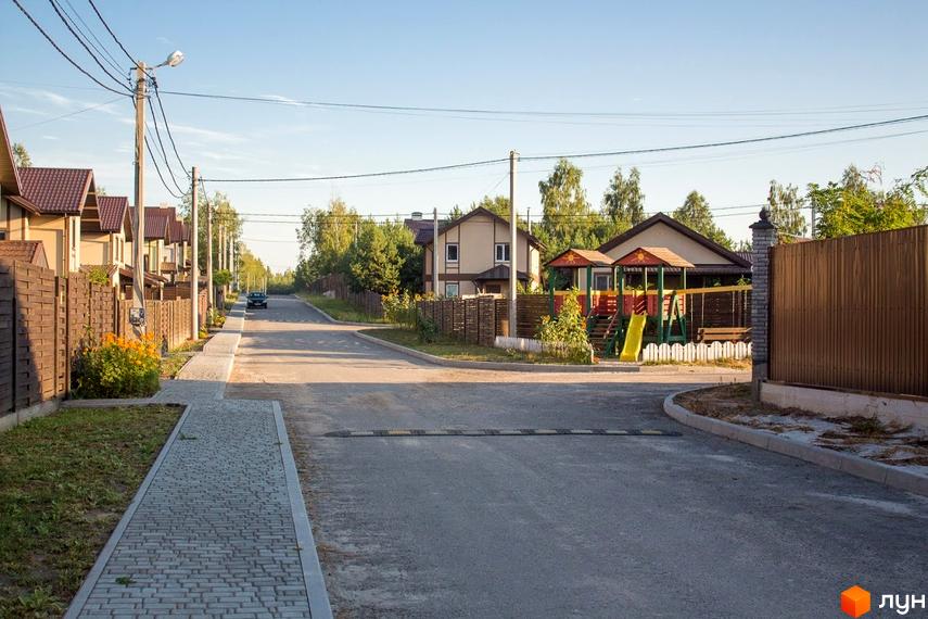 Вулиця в котеджному містечку Лісове озеро з будинками з коричневими дахами та парканами. На території є дитячий майданчик та зелені насадження.