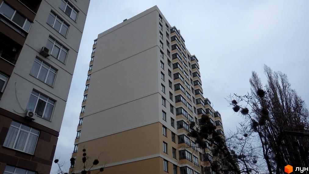 Вигляд на житловий комплекс на вул. Туманяна, 1а: високі будинки світлих та коричневих відтінків, з багатьма вікнами та балконами, поруч дерева.