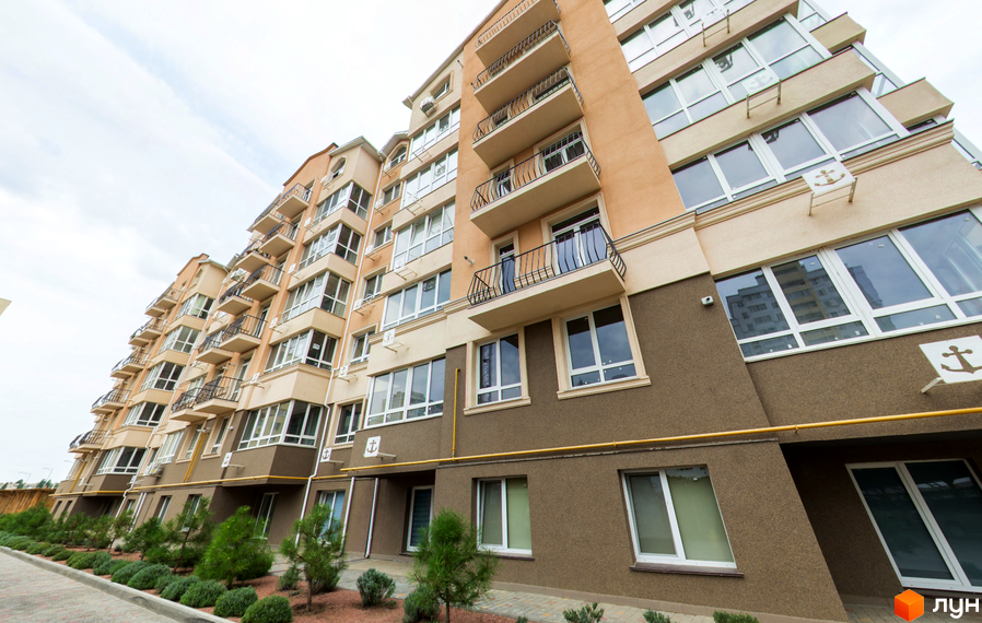 Житловий комплекс Якоря. Зовнішній вигляд багатоповерхового будинку з балконами та великими вікнами. Прибудинкова територія з зеленими насадженнями.