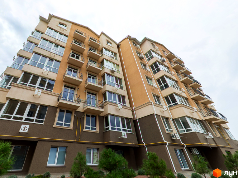 Висотна будівля Житлового комплексу Якоря з балконами та великими вікнами. На першому поверсі видно зелені насадження.