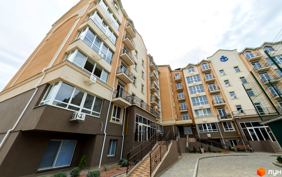 Зображення фасаду багатоповерхового будинку ЖК Якоря. Світлий фасад з великими вікнами та балконами. На прибудинковій території бруківка та сходи.