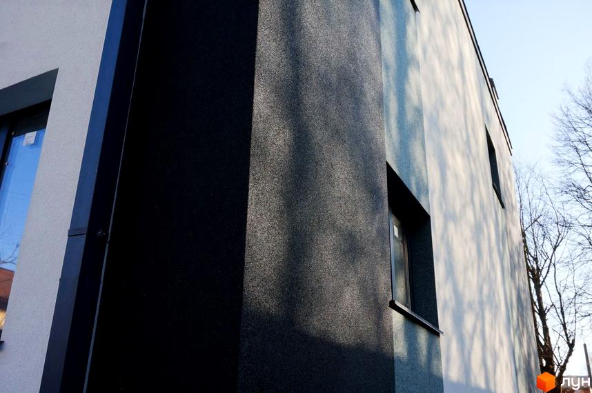 Фасад Таунхаус „Престиж“ з темним зернистим оздобленням та світлими стінами, на фоні видно вікна та безлисті дерева.