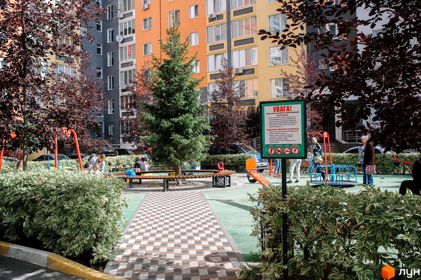 Житловий комплекс Синергія-2 з яскравими фасадами та дитячим майданчиком. На території комплексу є зелені насадження та місця для відпочинку.