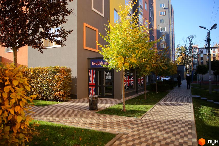 Фасад будівлі житлового комплексу з англійською школою на першому поверсі. Доглянута прибудинкова територія з бруківкою та зеленими насадженнями.