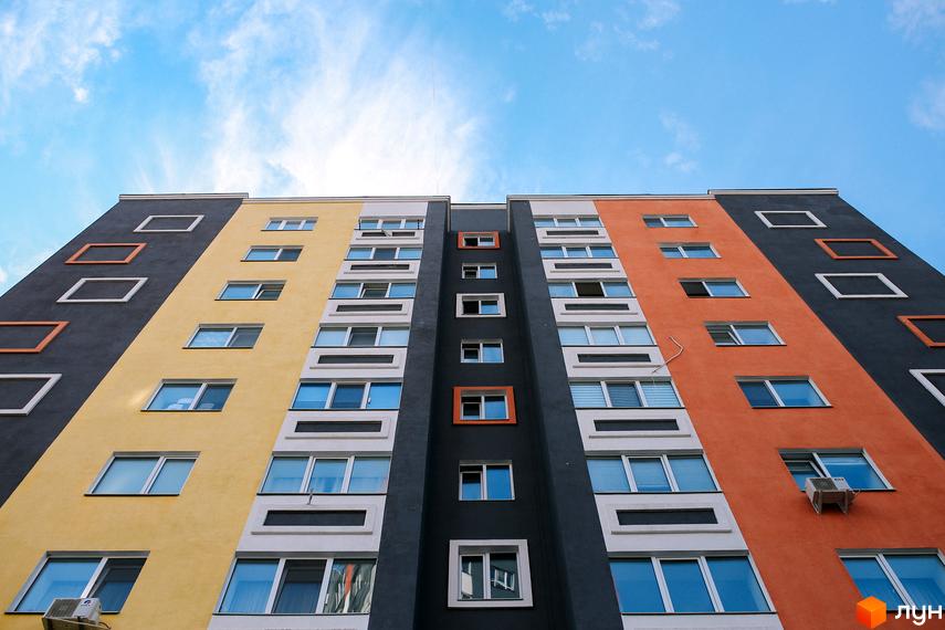 Висотна будівля ЖК Синергія-2 з різнокольоровими фасадами. На тлі блакитного неба розташований багатоповерховий будинок з великою кількістю вікон.