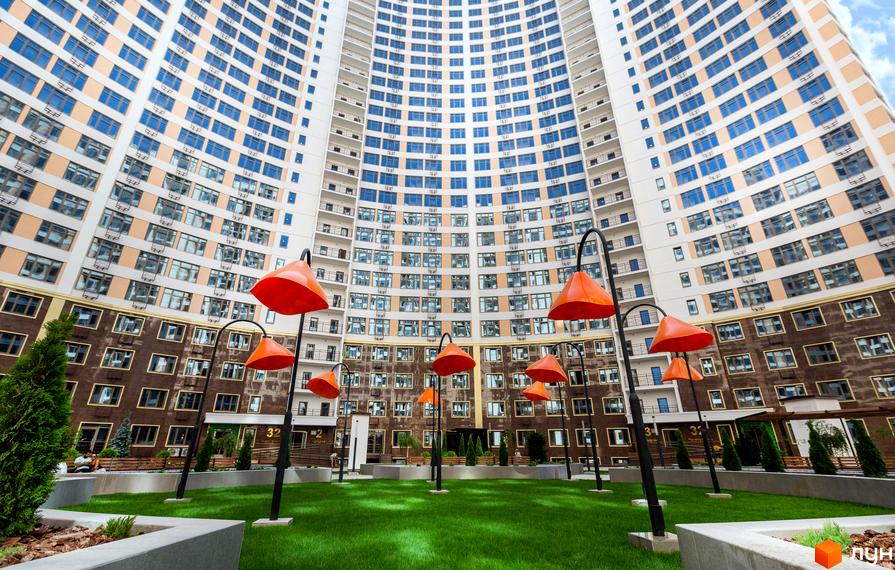 Житловий комплекс Тридцять друга перлина з фасадом з вікон та балконів, прибудинкова територія з газоном та ліхтарями.