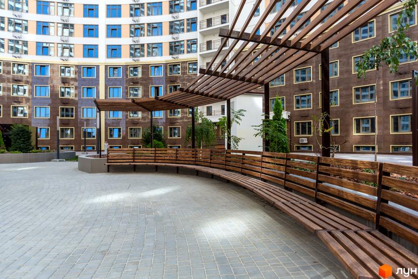 Житловий комплекс Тридцять друга перлина. Фасад будинку з численними вікнами та прибудинкова територія з дерев'яними лавками під навісом.