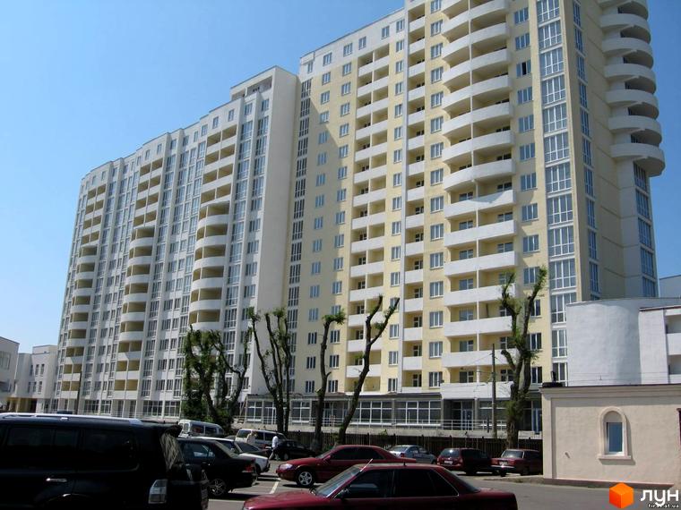 Житловий комплекс Тирас з сучасною архітектурою та відкритими балконами. Прибудинкова територія з автомобілями та зеленими насадженнями.