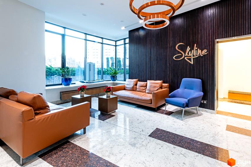 Інтер'єр холу новобудови ЖК Skyline з двома шкіряними диванами, кріслом та журнальними столиками. Велике панорамне вікно з видом на місто.