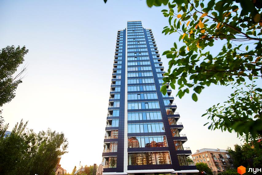 Новобудова ЖК Skyline – висотна будівля з панорамними вікнами та балконами, оточена зеленню. Зовнішній вигляд фасаду з темних панелей та скління.